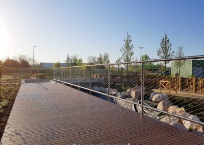 Garde-corps en filet inox 60x104 mm installé le long d’une passerelle en bois, assurant sécurité et discrétion.